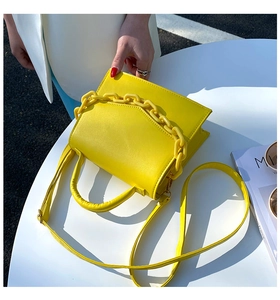 Detail of yellow crossbody square bag with a chunky decorative chain on white table