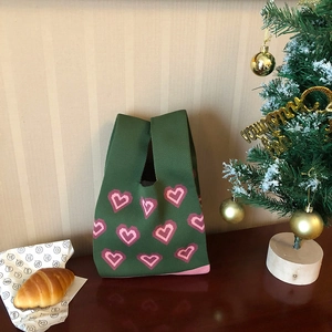 Close-up of green knit tote bag with pink heart patterns on a cozy festive table