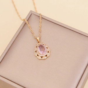 Golden teardrop necklace with pink center stone and crystal halo on beige jewelry box