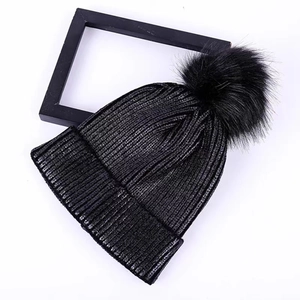 Flat lay view of a black knit beanie featuring a large fluffy pom-pom and ribbed texture