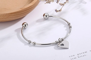 Detail of silver heart charm with cutout on stainless steel open bangle bracelet