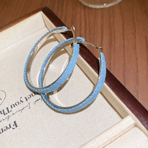 Details von blauen Denim-Stoff umwickelten geometrischen Creolen auf einer Schmuckschatulle