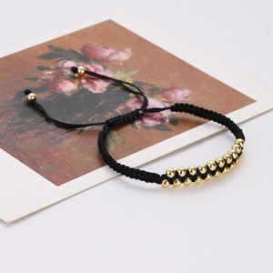 Detail of adjustable black woven bracelet with double row golden copper beads on white surface
