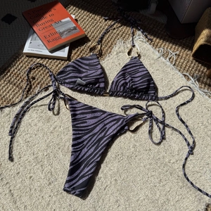 Detailed flat lay of zebra print bikini with golden rings on cream textured rug