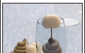 Funny poop shaped silicone tea infuser hanging on the edge of a clear glass tea cup