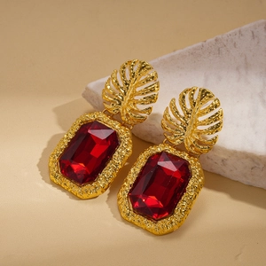 Detail of vintage gold earrings with red faceted stones on textured stone surface