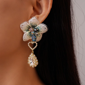 Gros plan de boucles d'oreilles fleur en tissu asymétriques avec pendentifs goutte en strass
