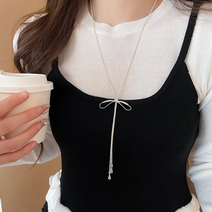 Collier élégant à nœud argenté avec de longs glands porté par un mannequin en gros plan