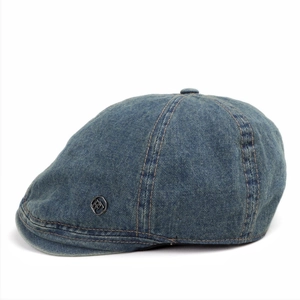Detail of washed denim flat cap with a round metal logo and precise stitching texture