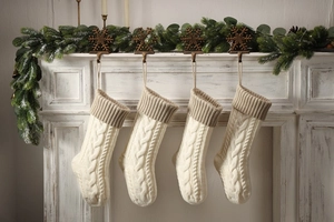 Detailed cable knit pattern on cream Christmas stockings hung on a festive fireplace