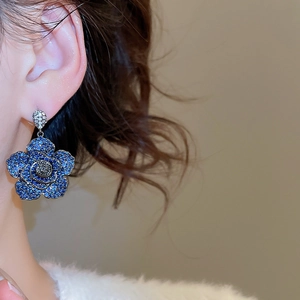 Close-up of elegant flower dangle earrings with blue pavé crystals worn by a model