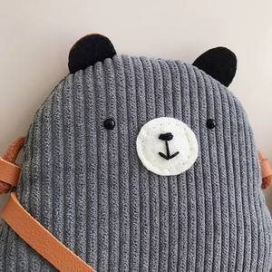 Detailed texture of grey corduroy teddy bear bag with fine embroidery and brown strap