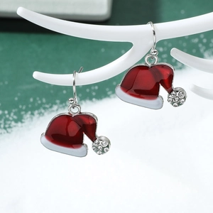 Close-up of red enamel Christmas hat earrings with white crystals on a festive branch