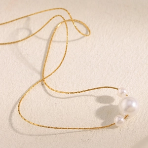 Close-up of elegant 18K gold plated chain with three faux pearls on textured background