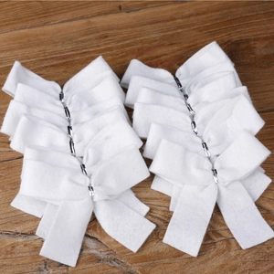 Bulk set of white felt Christmas tree bows arranged on a rustic wooden texture background