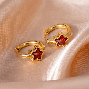 Macro shot of gold star hoop earrings with red star-shaped zircon on champagne silk fabric