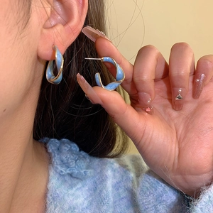 Elegant twisted blue enamel C-shaped earrings with gold trim worn by a model