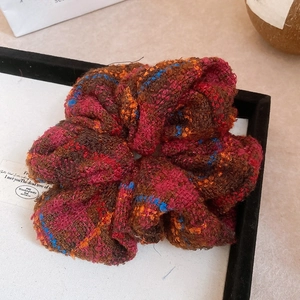 Détail d'un chouchou à carreaux marron rouge en tweed sur un plateau blanc élégant