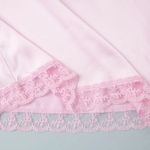 Macro shot of light pink satin fabric with delicate layered lace trim at the hemline