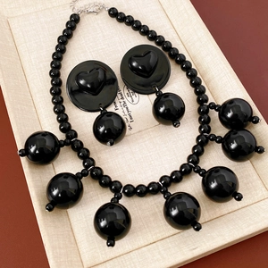 Detail view of black acrylic beaded tassel necklace and round earrings on gift card