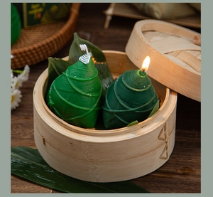 Detail of two green zongzi-shaped scented candles placed in a traditional wooden steamer