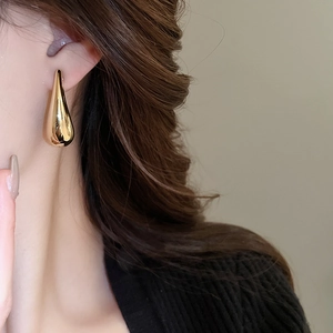 Gros plan sur des boucles d'oreilles gouttes d'or en forme de C portées par un mannequin