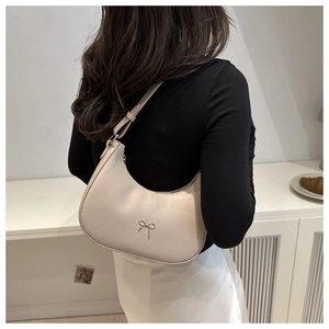 Close-up of a crescent-shaped beige shoulder bag with a delicate silver metal bow detail