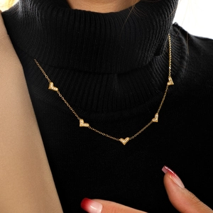 Detailed view of gold plated necklace with five micro-pave heart charms on black sweater