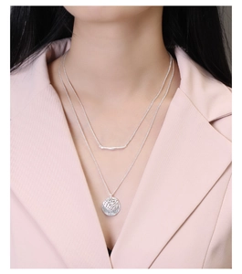 Close-up of double-layered silver necklace with bar and textured round coin pendant
