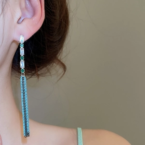 Detail of long fringe earrings featuring green gems and cascading black chains