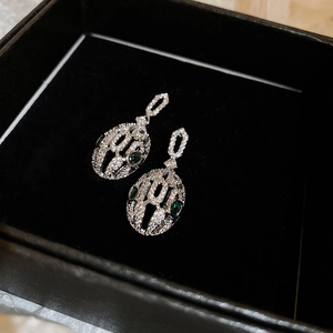 Detail of silver snake-head earrings featuring green emerald stones and white zircon stones
