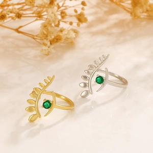 Detail of gold and silver feather rings with central green zircon in a soft light setting