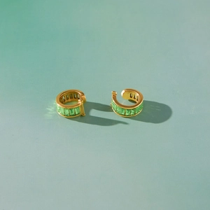 Boucles d'oreilles en acier doré et strass verts sur fond vert clair moderne