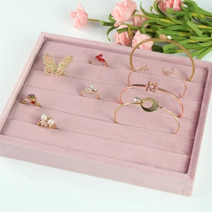 Pink velvet jewelry display tray with slots for rings and bangles on white background