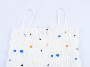 Dettaglio di spalline regolabili e tessuto a rete bianco plissettato a pois colorati