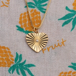 Détail du collier pendentif cœur avec texture rayons de soleil et petite pierre centrale