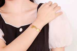 Detail of a gold heart charm bracelet with Love engraving on a model's wrist