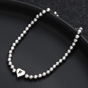 Beaded heart bracelet with silver round beads and black letter F charm on black background