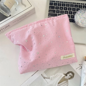 Pink canvas cosmetic bag with silver star patterns on a desk with makeup brushes