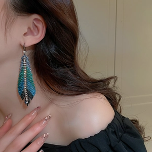 Macro detail of luxury feather drop earring featuring blue gradient rhinestones on model