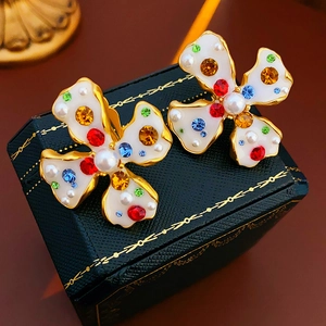 Detailed close-up of vintage gold earrings with white enamel and multicolor gemstone inlay