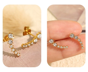Detailed view of curved gold stud earrings with white rhinestones and earlobe placement