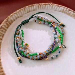 Detail of bohemian layered beaded bracelet with green and gold beads on ceramic plate
