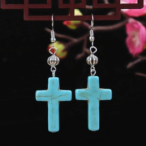 Detail of vintage turquoise cross earrings with silver hooks on an elegant dark background