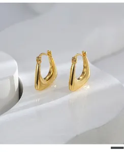 Polished gold U-shaped geometric earrings displayed on a white architectural pedestal