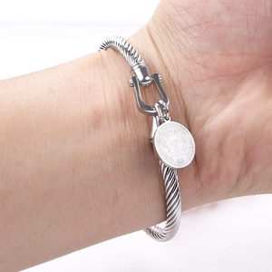 Detail of St. Benedict medal and U-shaped clasp on silver cable bangle worn on wrist