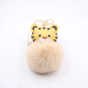 Close-up of cute cartoon tiger keychain with a soft beige faux rabbit fur pompom