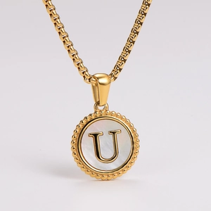 Detail of a golden round pendant necklace featuring white shell inlay and letter U