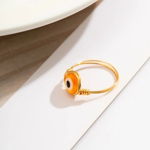 Macro detail of handmade gold wire-wrapped ring with orange evil eye gemstone bead