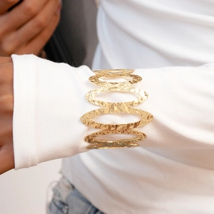 Detail of wide hollow oval gold cuff bracelet with hammered texture on white sleeve